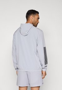 Αθλητικό ανοιχτό γκρι μπουφάν με κουκούλα, με μαύρες ρίγες στα μανίκια, σετ με αντίστοιχα υφασμένα σορτς.