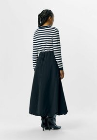 Robe longue avec un haut rayé blanc et bleu marine, et une jupe noire unie. Taille cintrée et encolure ronde, accompagée de bottines à la cheville.