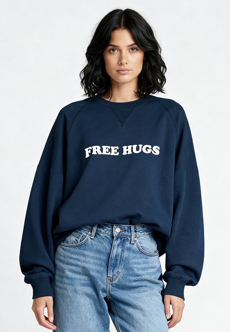 Sweatshirt bleu marine à manches raglan avec le texte blanc "FREE HUGS", associé à un jean taille haute bleu clair, offrant une coupe décontractée.