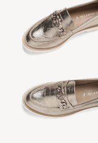 Metálfényű arany loaferek lánc díszítéssel a pánton, gumitalppal és sima textúrával; kerek orrú és slip-on kialakítású.