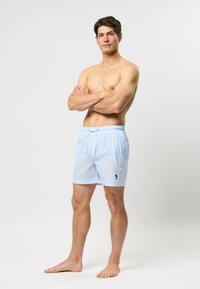 Modri karo kopalni šorts s elastiko in vrvico za zategovanje. Ima stranske žepe in majhen črn logotip na strani.