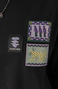 Czarna tkanina z trzema naszywkami: logo węża, ptaki w fioletowych ramach oraz gepard w kropki na zielonym tle z fioletową ramką.
