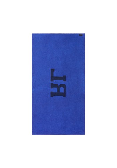 Μπλε πετσέτα με απαλή υφή, με μεγάλα μαύρα γράμματα "BT" εκτυπωμένα κεντρικά. Τελειωμένες άκρες και μια μικρή ετικέτα μάρκας στη γωνία.