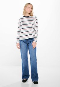 Gestreept breisweater met horizontale strepen in roze, blauw en marineblauw op een witte achtergrond. Gepaard met wijde blauwe jeans.