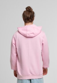 Sudadera rosa con capucha, de mangas largas y corte holgado. Textura suave, costuras acabadas y un detalle de bolsillo trasero estándar.