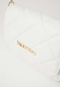 White quilted leather Valentino purse with gold chain strap and gold logo lettering on front flap.