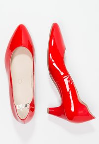 Chaussures à talons hauts en cuir verni rouge avec bout pointu, bord festonné et petit talon large. Fini lisse et brillant.