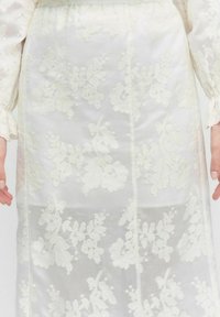 Valkoinen broderi-mekko, jossa on kukkakuvioita, pitkät hihat, kerrostettu vyötärö ja läpikuultava, teksturoitu pinta.