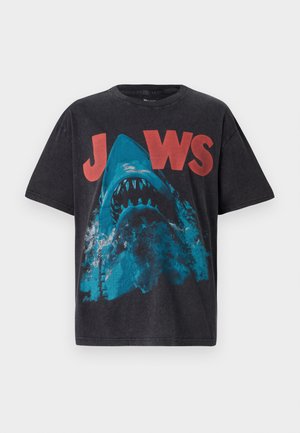 Black t-shirt with short sleeves featuring a blue shark graphic and red "JAWS" text on the front. Made of cotton with a standard fit.
