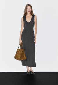 Robe sans manches grise avec un décolleté en V profond, une longueur au genou et une coupe ajustée, accompagnée d'un sac à main en daim marron et de chaussures grises.