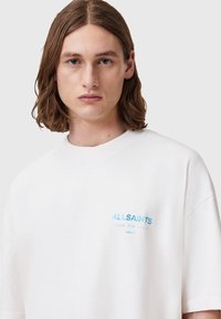 Hvid oversized bomulds T-shirt med blå "ALLSAINTS" tekst på venstre bryst. Glat tekstur og afslappet pasform.