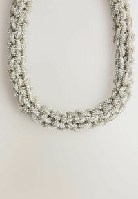 Kausēta kaklarota no mirdzošām sudraba pērļu bumbām; gluda tekstūra ar vairākiem savītiem pavedieniem, veidojot noteiktu formu.