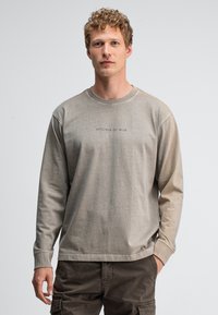 Langärmliger Baumwollpullover in hellem Beige mit gerippten Bündchen. Mit "BUTCHER OF BLUE" auf der Brust bedruckt. Lockerer Schnitt.