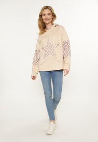 Ljus persiko hoodie med en stor stjärndesign och blommönster på ärmarna. Kombineras med blå skinny jeans och vita sneakers.