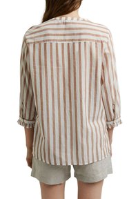 Blouse rayée en coton beige clair et blanc, manches longues avec des poignets à volants, détail de empiècement au dos et ourlet arrondi.