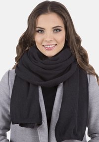 Sort uld tørklæde viklet omkring halsen, med en blød, tekstureret finish. Enderne hænger let under kraven på en grå frakke.