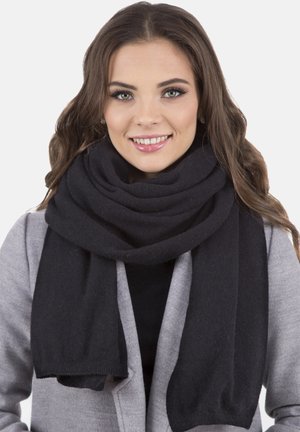 Černá vlněná šála omotaná kolem krku, s jemnou, strukturovanou úpravou. Konec šály lehce visí pod límcem šedého kabátu.