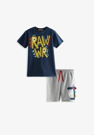 Marineblauwe T-shirt met een "RAWR" grafiek in geel en rood, gecombineerd met grijze shorts met een krokodilprint en een rode koord.