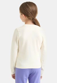 Top crema a maniche lunghe realizzato in tessuto morbido, con scollo tondo semplice e design posteriore liscio e senza decorazioni.