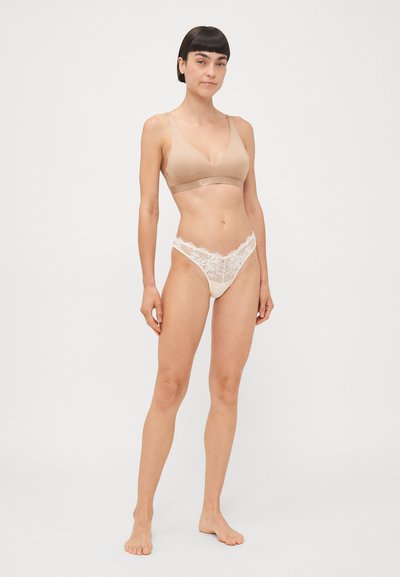 Beige bralette with a smooth finish and adjustable straps, paired with cream lace thong featuring floral accents and a low-rise fit.