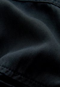 Tessuto nero con fine trama a coste, caratterizzato da un sottile lucido. La visione ravvicinata mostra i dettagli delle cuciture e le pieghe del tessuto, senza motivi né decorazioni.