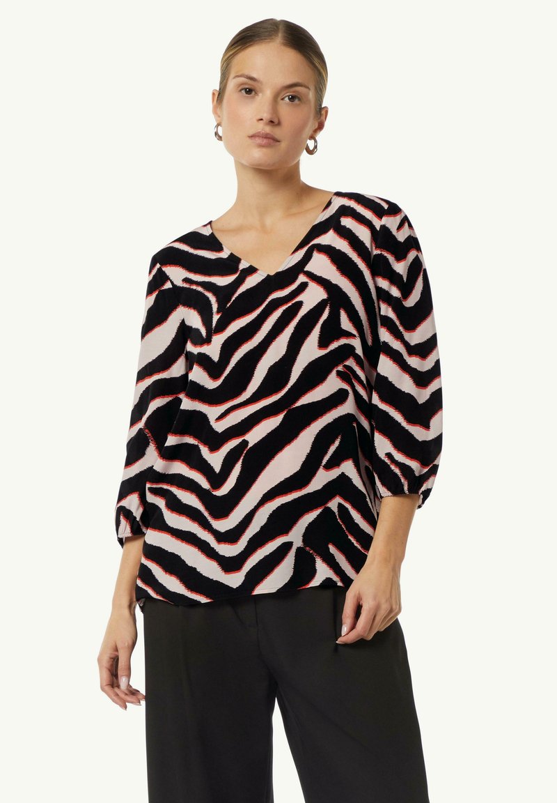Schwarzes und pinkes Oberteil mit Zebra-Muster. V-Ausschnitt-Design, dreiviertel Ärmel und lockere Passform. Glatte Stofftextur.