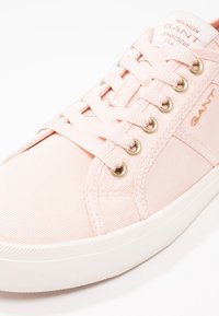 Sneakers GANT rose clair avec semelle blanche, tige en tissu, lacets roses et œillets dorés, affichant le logo sur la languette et sur le côté.