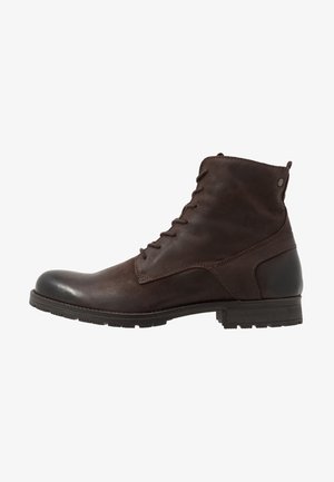 Bottine montante en cuir marron foncé à lacets, avec un petit talon et une semelle en caoutchouc texturée, montrée de profil sur fond blanc.