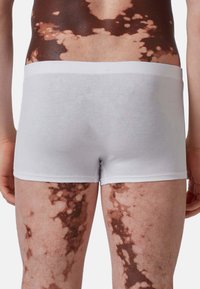 Boxer da uomo bianchi in cotone con una cintura morbida, indossati da una persona che mostra la pelle con una texture a motivi marrone e beige sulle gambe.