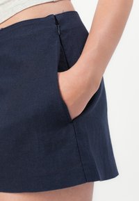 Navy blue skirt with a textured fabric, featuring a side pocket and a concealed zipper. Tailored, fitted design with a straight hem.