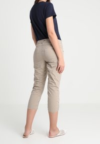 Beige cropped broek gemaakt van zachte stof met een slim fit. Heeft zijzakken en geplooide details langs de benen. Gecombineerd met een navy top.