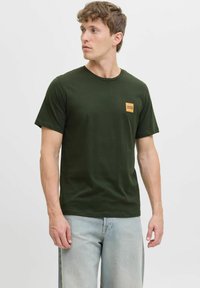 Grünes Baumwoll-T-Shirt mit Rundhalsausschnitt, kurzen Ärmeln und einem kleinen orangefarbenen quadratischen Logo auf der linken Brust. Hat eine lässige Passform.
