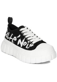 Sneaker nera in tela con suola in gomma bianca spessa, caratterizzata da un audace design con testo bianco, punta tonda e lacci bianchi.