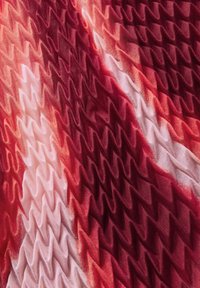 Tejido texturizado en gradientes de rojo profundo y rosa suave. El patrón ondulado crea pliegues dimensionales. Material ligero con un acabado suave.