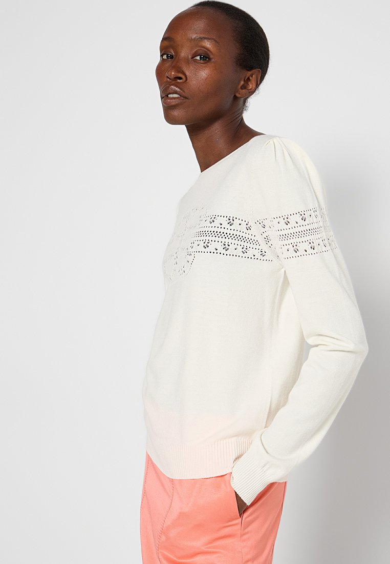 Helle beigefarbene Pullover mit strukturiertem horizontalem Streifendetail, gerippten Bündchen und Saum. Kombiniert mit korallenfarbenen Hosen, die eine lockere Passform zeigen.