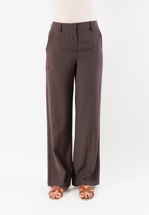 Pantaloni larghi marroni con una superficie liscia, due tasche laterali e una parte frontale piatta. Abbinati a sandali piatti color cammello.