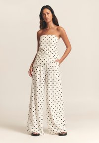 Valged täpilised rihmadeta top ning laia lõikega püksid, mõlemal mustad täpid. Lahtine lõige taskutega, tekstuurse kangaga. Mustad sandaalid.