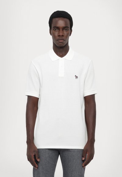 Camisa polo blanca con cuello acanalado y mangas cortas. Presenta un pequeño logotipo bordado en el lado izquierdo del pecho. Tejido suave y liso.