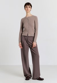 Cardigan beige a maglia con texture a coste, chiusura con bottoni e scollo arrotondato, abbinato a pantaloni taupe a gamba larga.