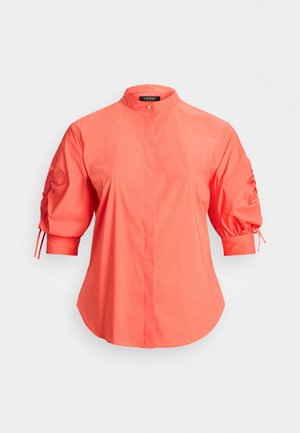 Koraalroze blouse met mandarinnek, vooraan verborgen knoopsluiting en geplooide ellebooglange pofmouwen met strikjes.