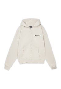 Sudadera beige con cremallera, capucha con cordón, bolsillos tipo canguro y puños acanalados. Presenta un pequeño logo negro en la parte delantera. Tejido de textura suave.