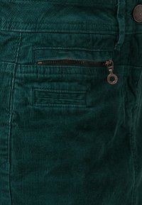 Tessuto in corduroy verde acqua con righe verticali, dotato di tasca con zip e di una tasca piatta sopra. Dettaglio con bottone in metallo sulla vita.