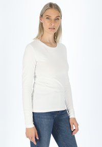 Witte, aansluitende t-shirt met lange mouwen van soepel katoen, met een ronde halslijn en naadloze manchetten, gecombineerd met blauwe denim jeans.
