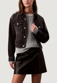 Černá džínová bunda se stříbrnými knoflíky, předními kapsami a krátkým střihem. Nasažená přes šedý žebrovaný svetr a černou koženou sukni.