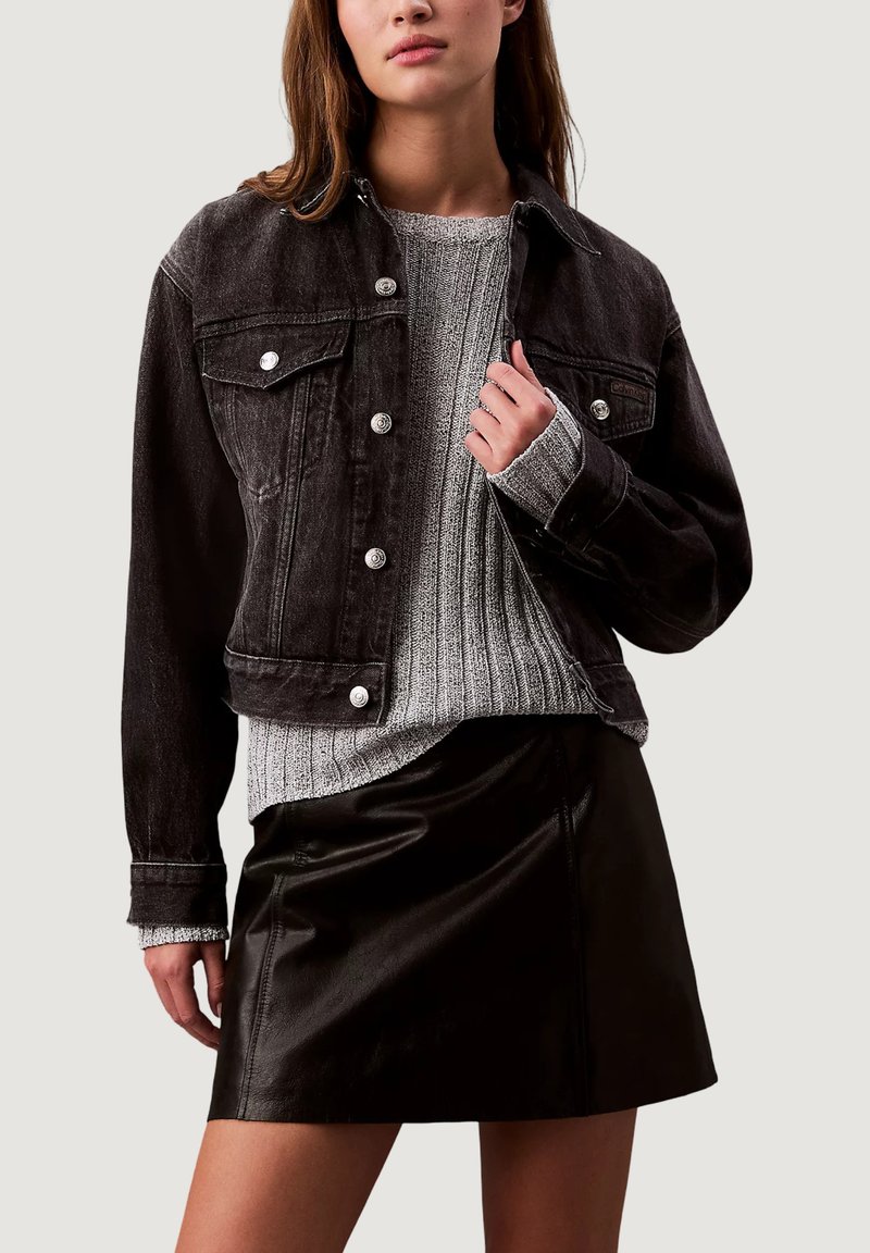 Černá džínová bunda se stříbrnými knoflíky, předními kapsami a krátkým střihem. Nasažená přes šedý žebrovaný svetr a černou koženou sukni.