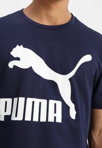 Camiseta de algodón azul marino con un destacado logo blanco de Puma y texto. Mangas cortas, cuello redondo, textura suave, diseño casual.