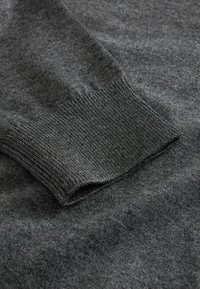 Dunkelgrauer Pullover, hergestellt aus weichem Strickmaterial. Verfügt über ein geripptes Bündchen mit glatter Textur und minimal sichtbar gemustert.