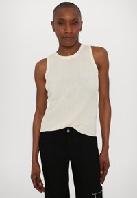 Top de tirantes blanco con textura acanalada, hecho de una tela ligera, que presenta un cuello redondo y un diseño sin mangas, combinado con pantalones negros de cintura alta.