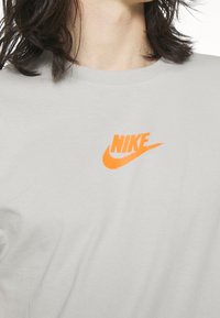 Close-up of a person wearing a light gray shirt with an orange Nike logo on the chest, shoulder-length dark hair visible.