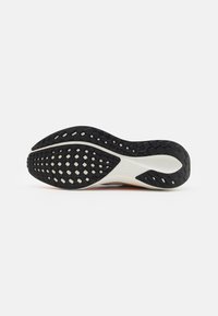 Black rubber sole with textured grip pattern, featuring a white midsole and slight orange accent at the back. Smooth, rounded shape.